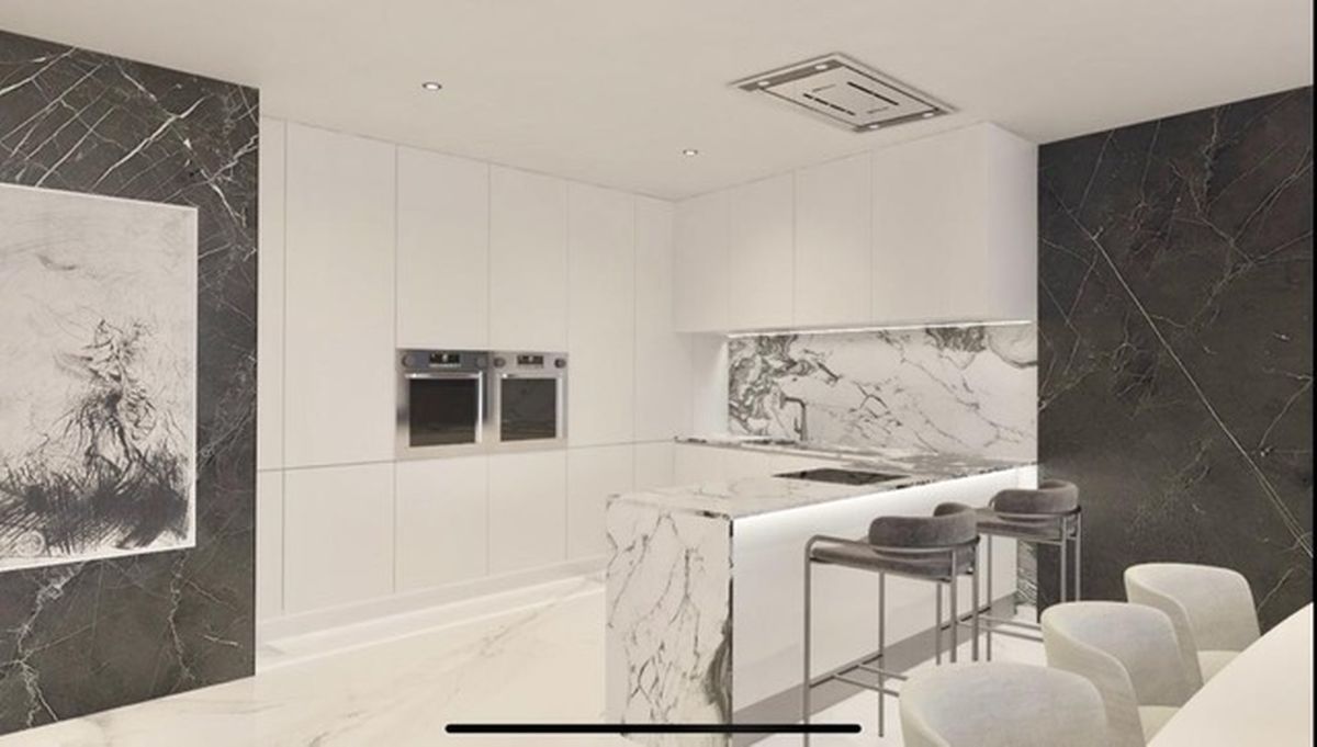Moderne keuken met minimalistische witte kasten, een marmeren watervaleiland, geïntegreerde dubbele ovens en donkere marmeren wandpanelen met inbouwspots.