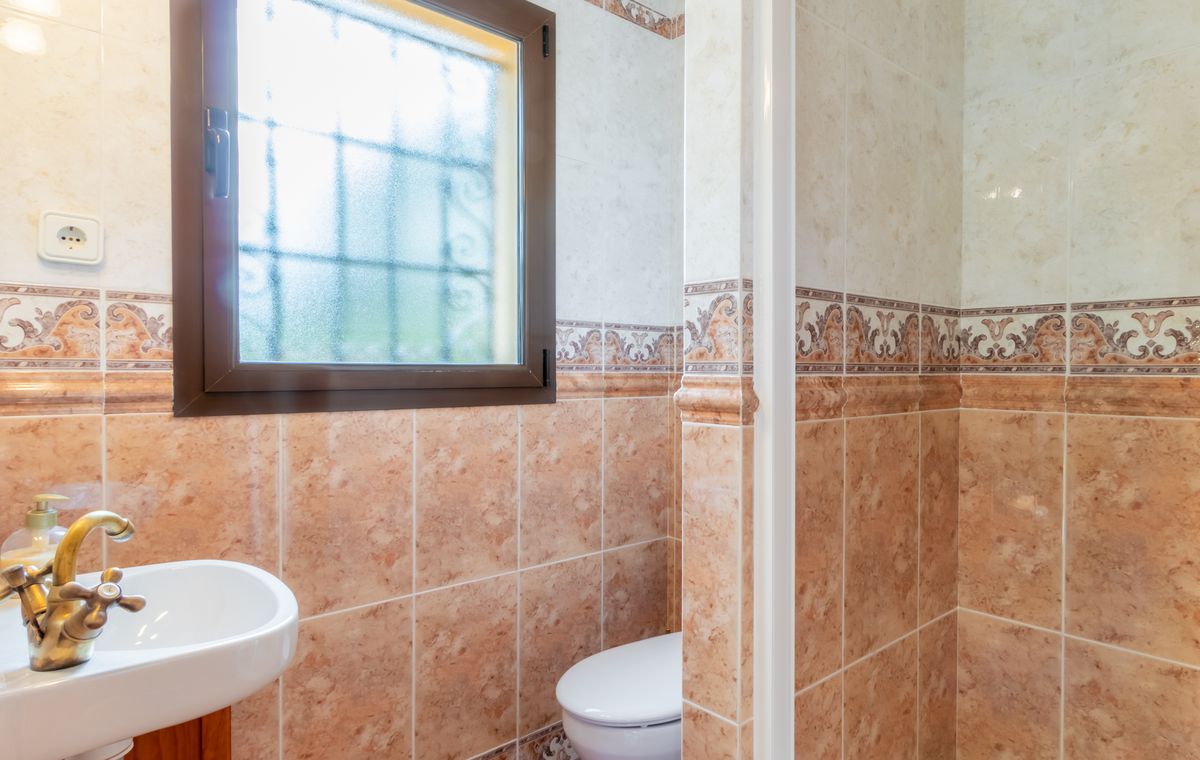 Badkamer met gemarmerde tegels in terracotta tinten, een klassieke koperen kraan en een raam met matglas en veiligheidsrooster voor privacy.