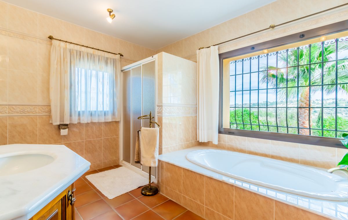 Badkamer met ingebouwd ligbad onder het raam, aparte douchecabine, wit marmeren wastafelblad en rustieke terracotta vloertegels.