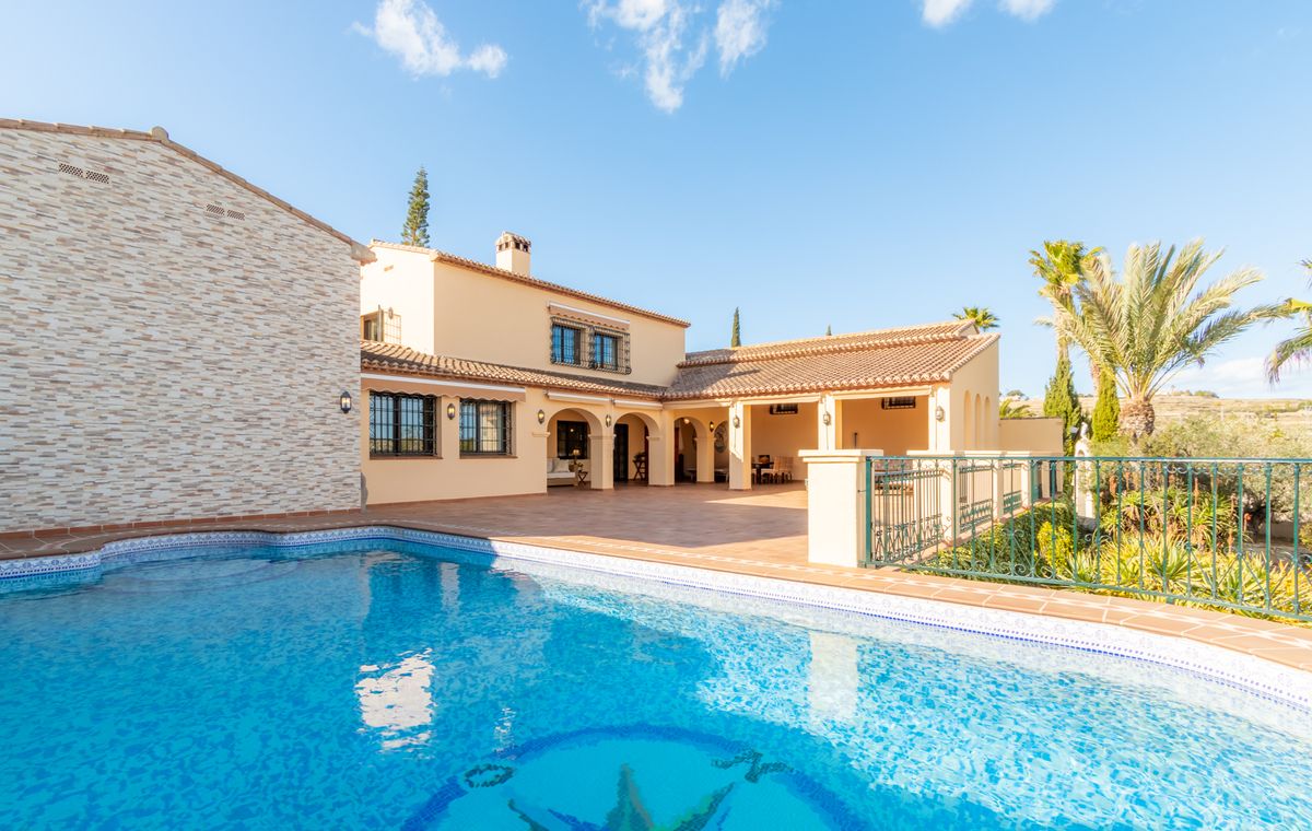 Exterieur van een mediterrane villa met een mozaïekzwembad, een ruim terracotta terras en een overdekte veranda met bogen.