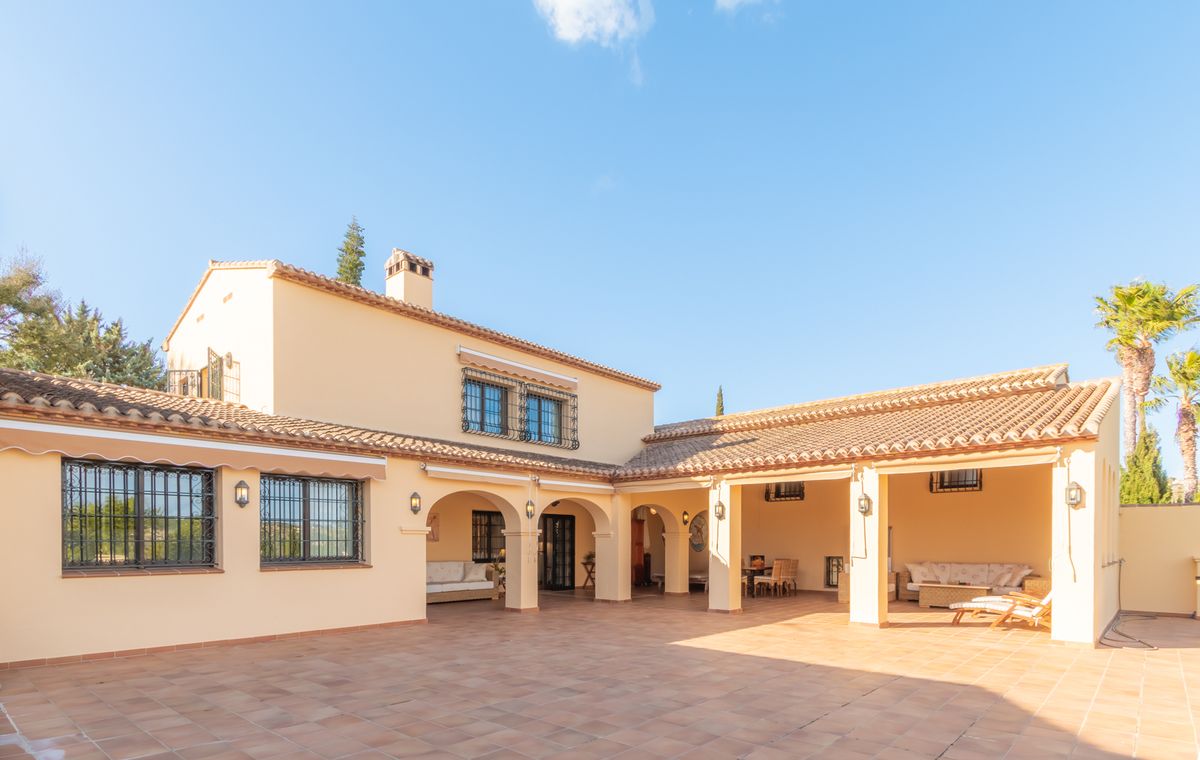 Exterieur van een mediterrane villa met een ruim terras van terracotta tegels, overdekte terrassen met bogen en zithoeken tegen een crèmekleurige gevel.