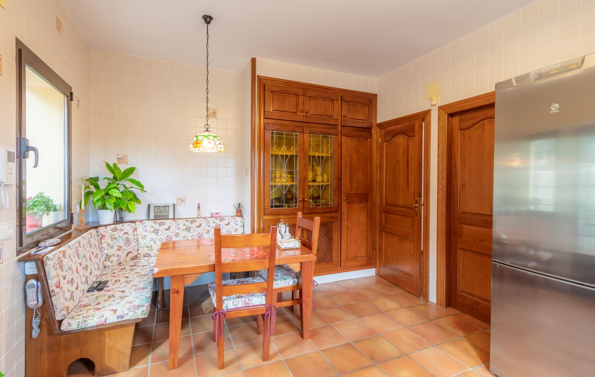 Keuken-eethoek met ingebouwde houten bank, terracotta tegelvloer en op maat gemaakte houten kasten met glas-in-lood details.