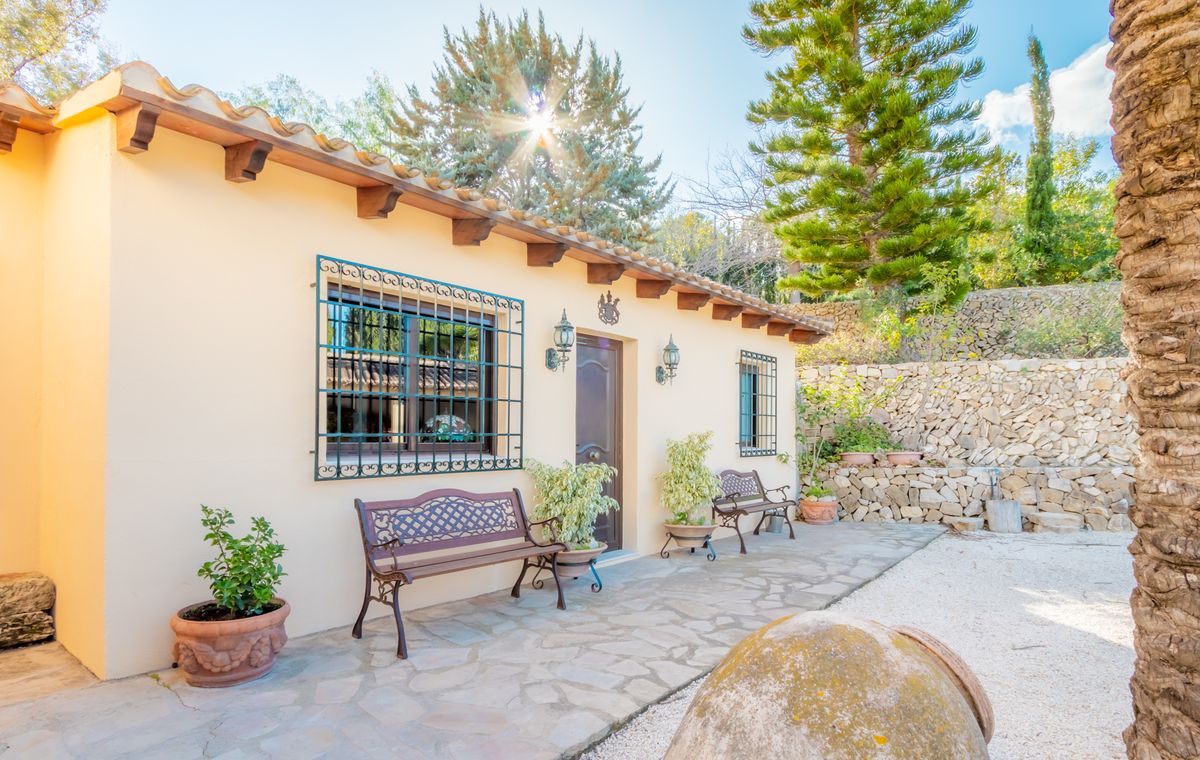 Mediterrane gevel met houten balken, smeedijzeren raamroosters en een terras van natuursteen voorzien van sierlijke banken en beplanting.
