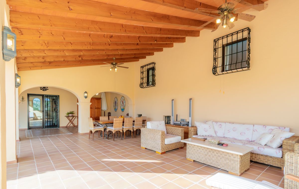Overdekt terras met een plafond van houten balken, terracotta vloertegels en een zithoek met rieten meubilair en eethoek.