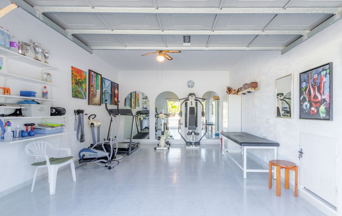 Privé-fitnessruimte in een omgebouwde garage met tegelvloer, uitgerust met cardio-apparatuur, een krachtstation en een behandeltafel.