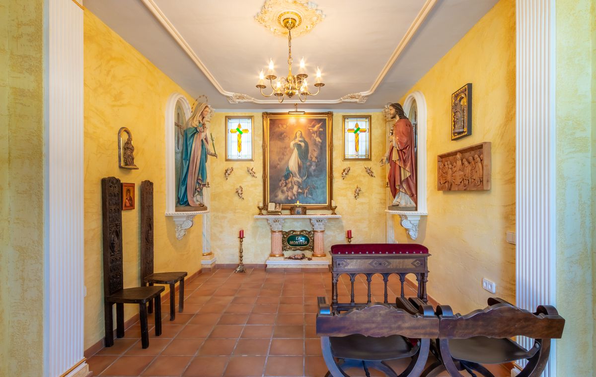 Privékapel met geel getextureerde muren, terracotta vloer, centraal altaar met religieuze schilderijen, nissen met beelden en klassiek houten meubilair.