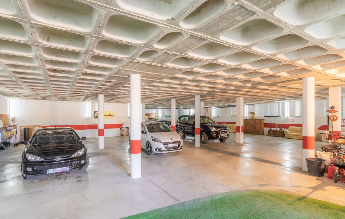Ruime ondergrondse garage met een karakteristiek wafelplafond van beton, witte steunpilaren met rode markeringen en voldoende parkeergelegenheid voor meerdere auto's.