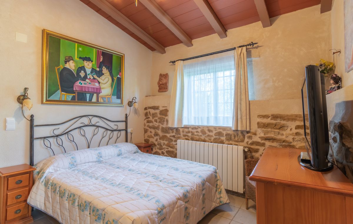 Rustieke slaapkamer met een smeedijzeren bed, muren van natuursteen en een houten balkenplafond. Een groot figuratief schilderij en een houten dressoir sieren de kamer.
