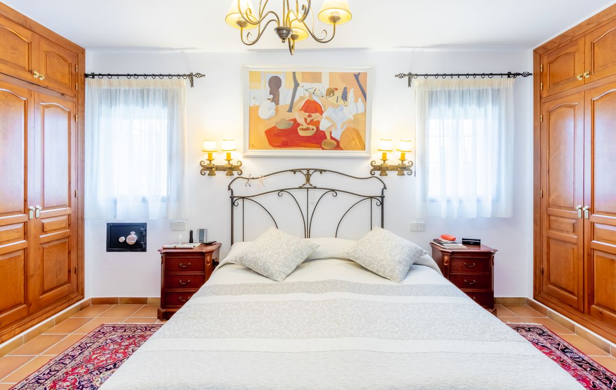 Slaapkamer met een smeedijzeren hoofdbord, symmetrische houten inbouwkasten en een terracotta tegelvloer. Voorzien van wandlampen en een ingebouwde kluis.