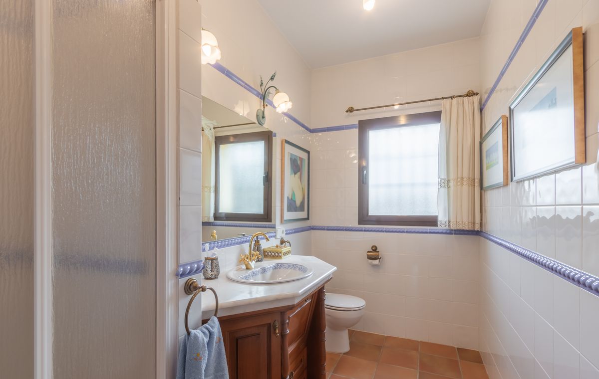 Traditionele badkamer met witte wandtegels met blauwe randen, een houten wastafelmeubel met marmeren blad en terracotta vloertegels.