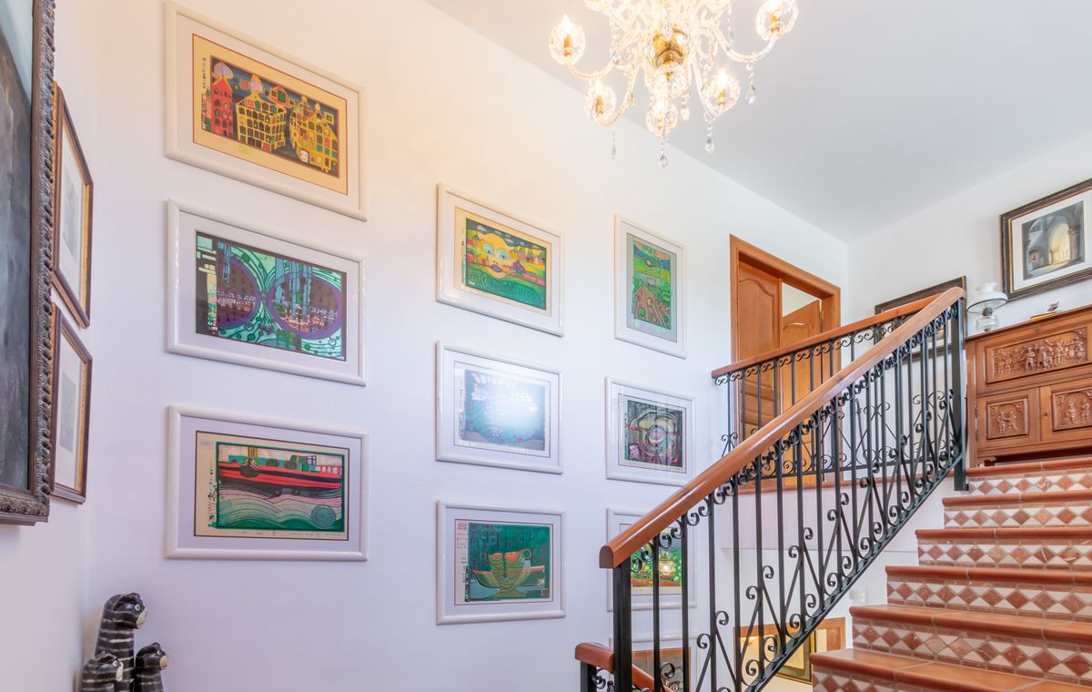 Trap met terracotta treden en gedecoreerde stootborden, een smeedijzeren leuning en een galerijwand met kunstwerken verlicht door een kristallen kroonluchter.