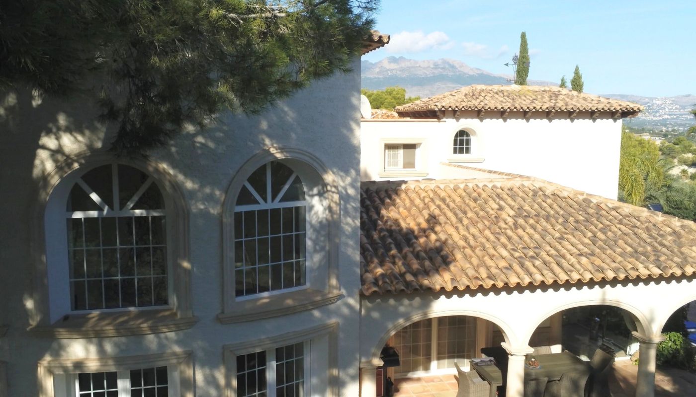 Exterieur van een mediterrane villa met terracotta pannendaken, boogvensters en een overdekt terras met uitzicht op de bergen.