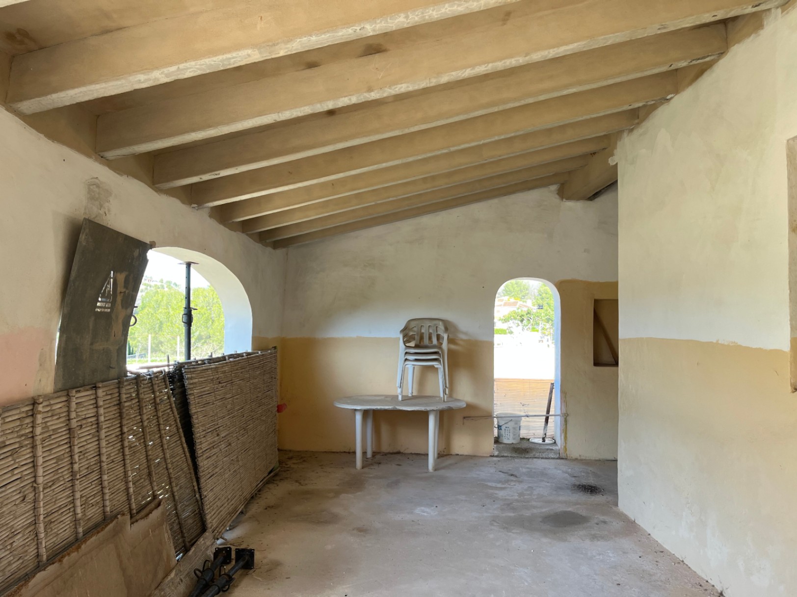 Binnenruimte met schuin plafond voorzien van houten balken en boogvormige openingen. De kamer verkeert in originele staat en is klaar voor renovatie.