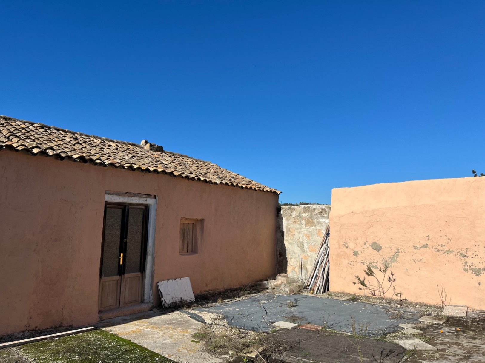 Buitenaanzicht van een traditionele finca met een terracotta gevel, pannendak en houten deur, klaar voor een volledige renovatie in Jávea.
