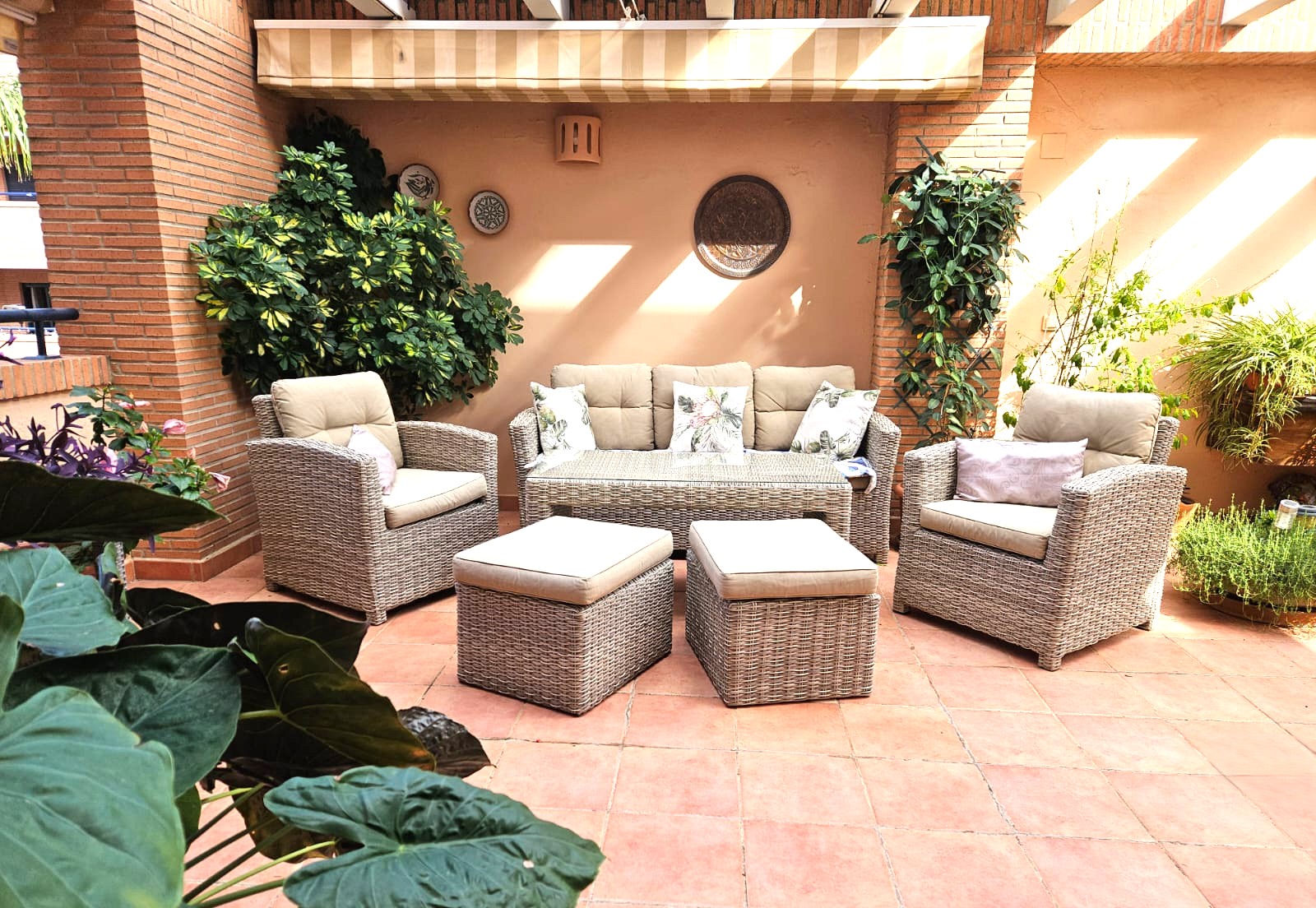 Privéterras met terracotta vloertegels, een loungeset van grijs gevlochten rotan en een uitschuifbaar zonnescherm, omgeven door weelderige beplanting.