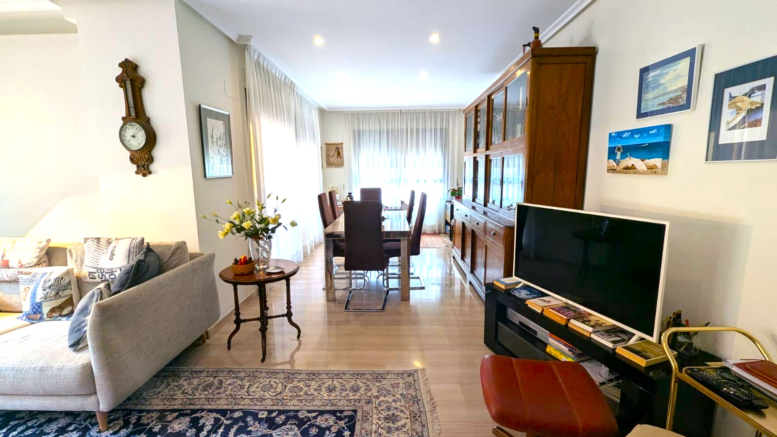 Ruime woon-eetkamer met gepolijste marmeren vloer, een grote houten vitrinekast en een glazen eettafel onder subtiele plafondspots.