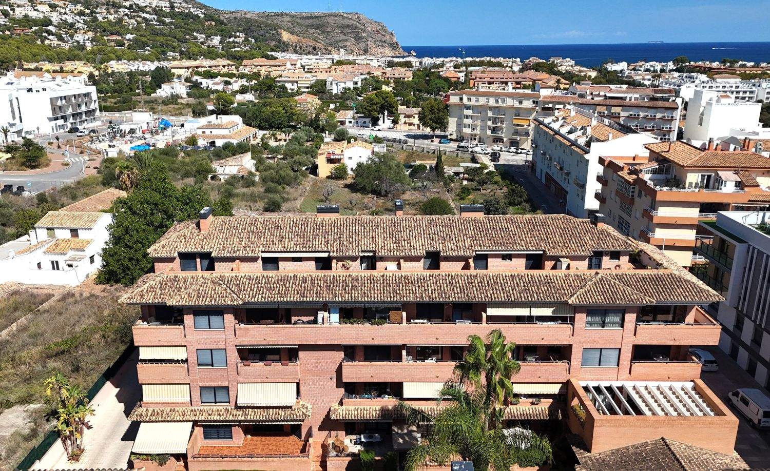 Verhoogd vooraanzicht van een bakstenen appartementencomplex met terracotta daken, balkons met zonneschermen en uitzicht over Jávea en de Middellandse Zee.