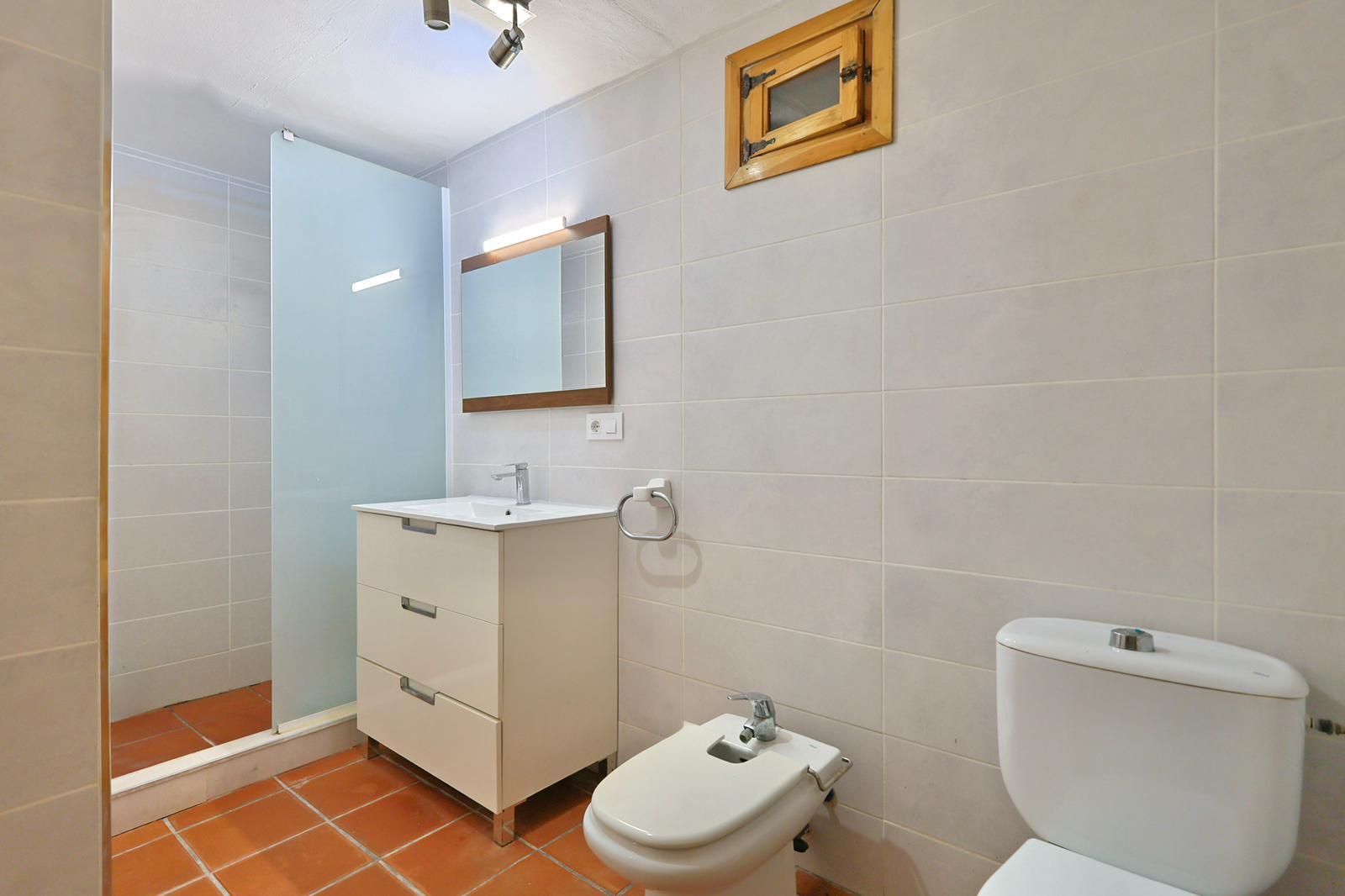 Badkamer met terracotta vloertegels, wit wastafelmeubel met drie laden, bidet en inloopdouche met matglazen wand.