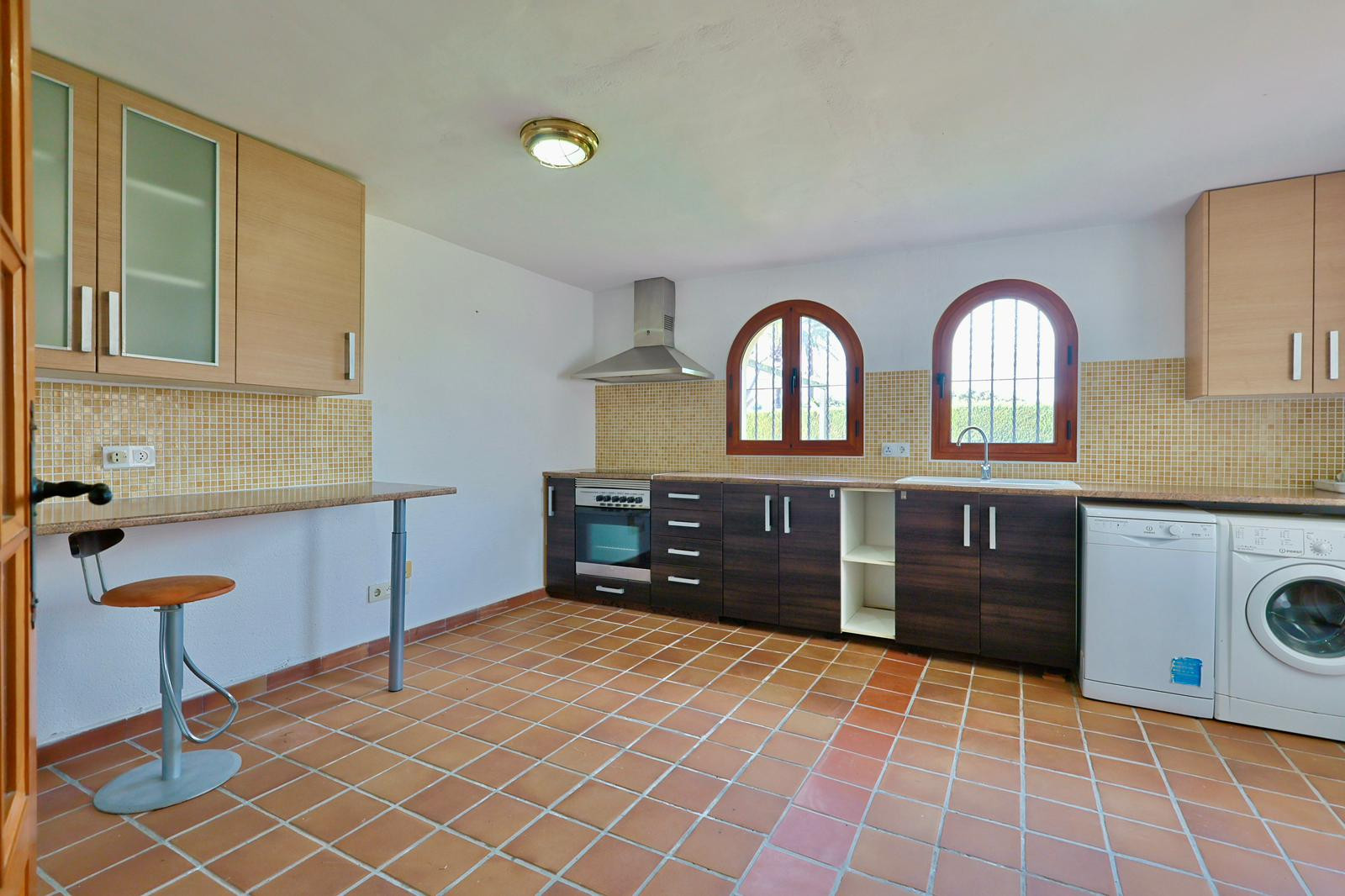 Functionele keuken met terracotta tegelvloer, tweekleurige kasten, houten boogvensters en inbouwapparatuur. Inclusief ontbijtbar en beige mozaïek achterwand.