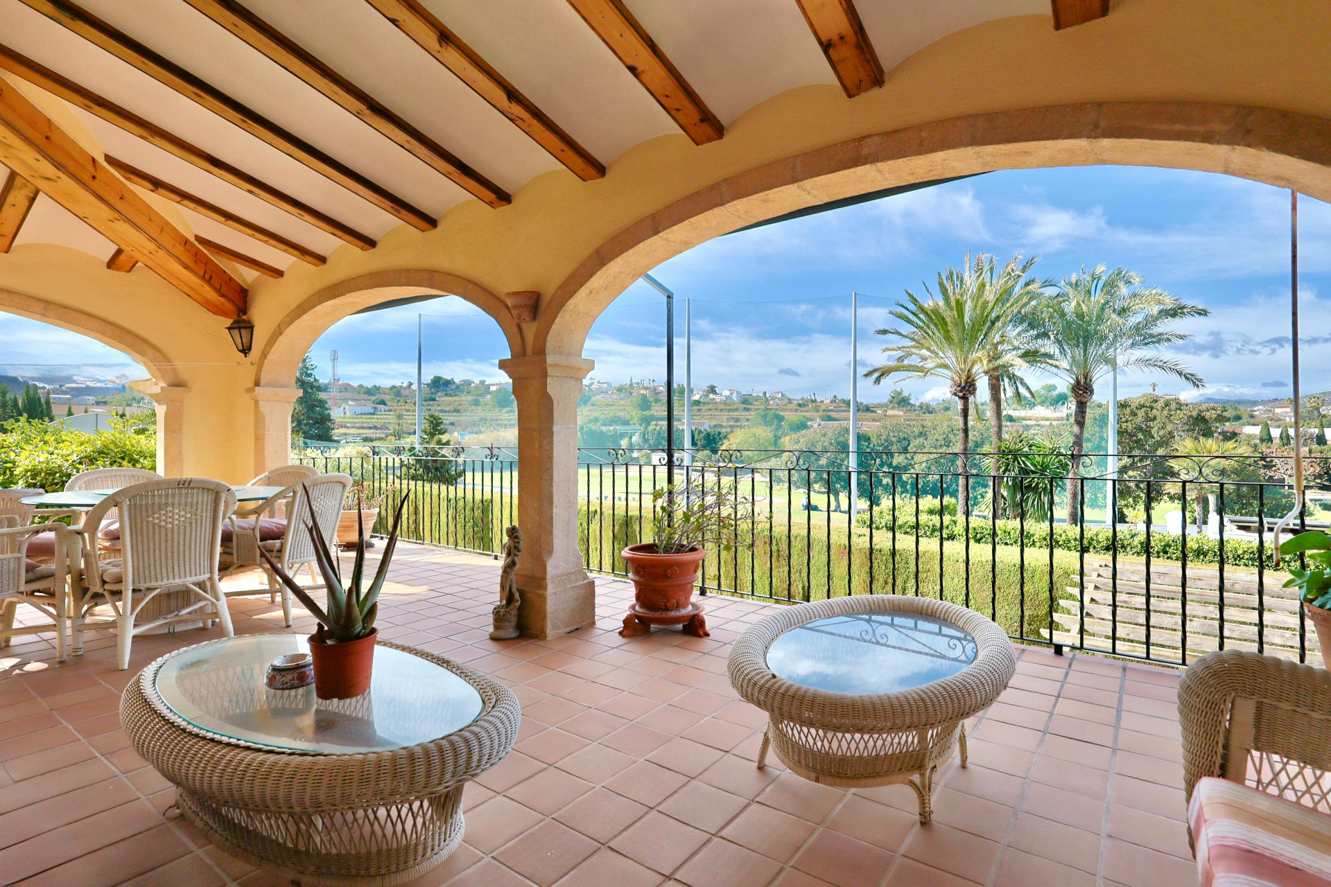 Overdekt terras met stenen bogen, houten balken en terracotta tegels, met een weids uitzicht over de golfbaan en de omliggende mediterrane natuur.