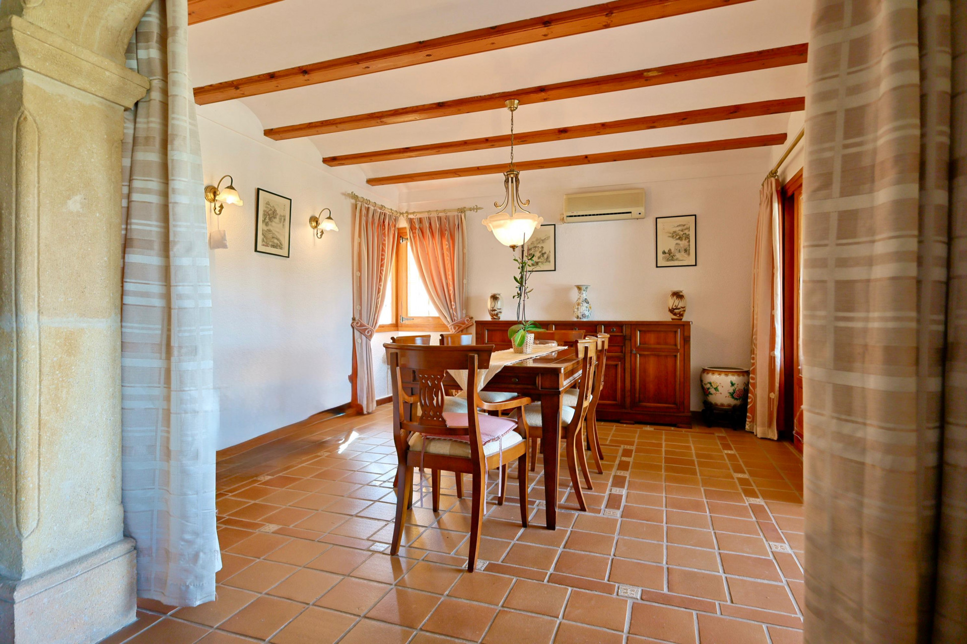 Rustieke eetkamer met houten balkenplafond, terracotta vloer en een boog van Tosca-steen. Ingericht met een massief houten eethoek en dressoir.