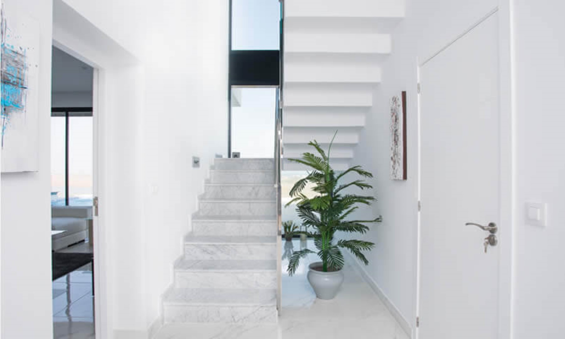 Minimalistische entreehal met een marmeren trap en witte zwevende treden, verlicht door een hoog verticaal raam dat zorgt voor veel natuurlijk licht.