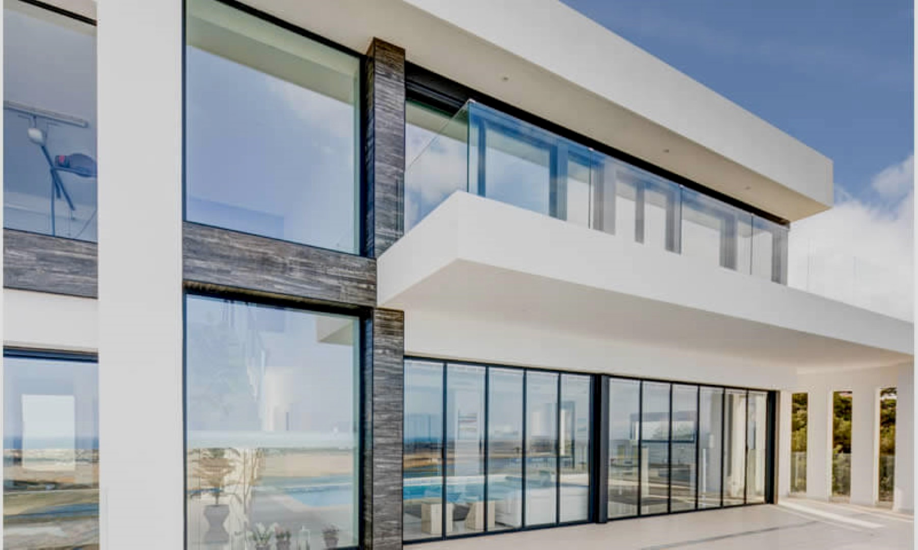 Moderne gevel met kamerhoge glazen puien, donkere natuurstenen accenten en een balkon op de bovenverdieping met een glazen balustrade.