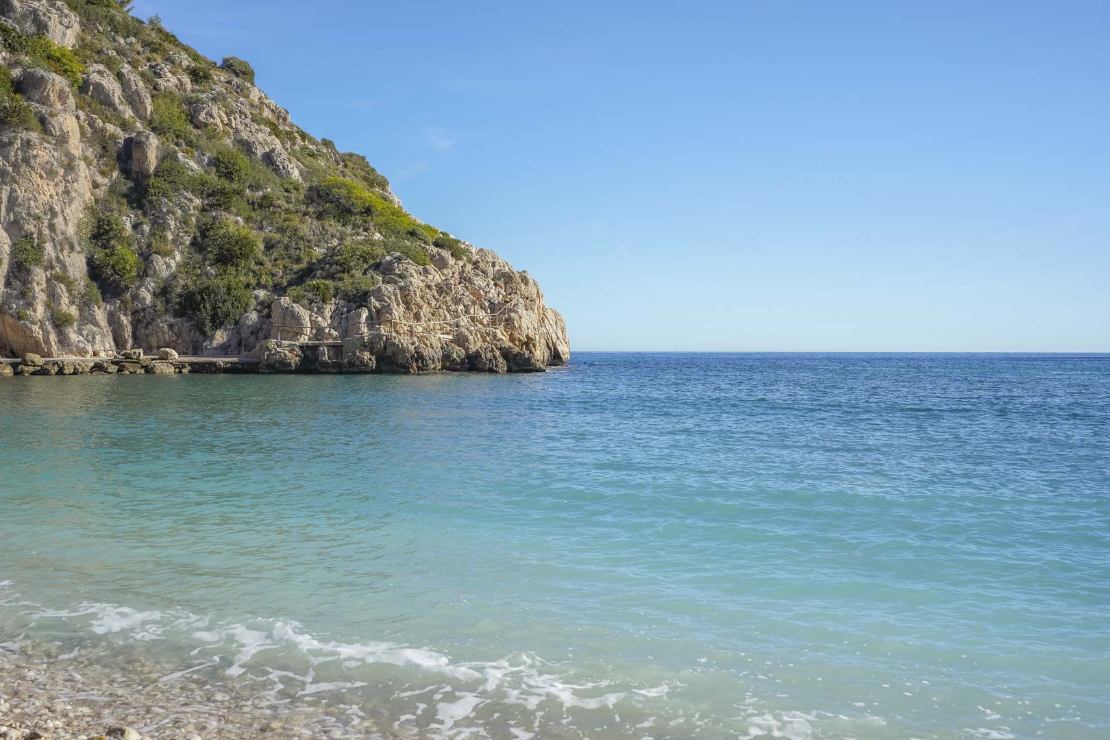 Uitzicht op de baai van Granadella in Jávea, gekenmerkt door kristalhelder turquoise water, een kiezelstrand en steile rotswanden met mediterrane begroeiing.