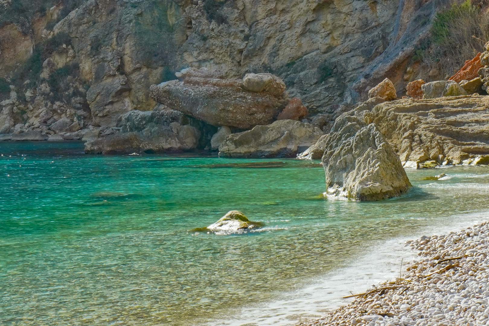 Uitzicht op de baai van Granadella met kristalhelder turquoise water en een kiezelstrand, omgeven door de ruige kliffen van Jávea.