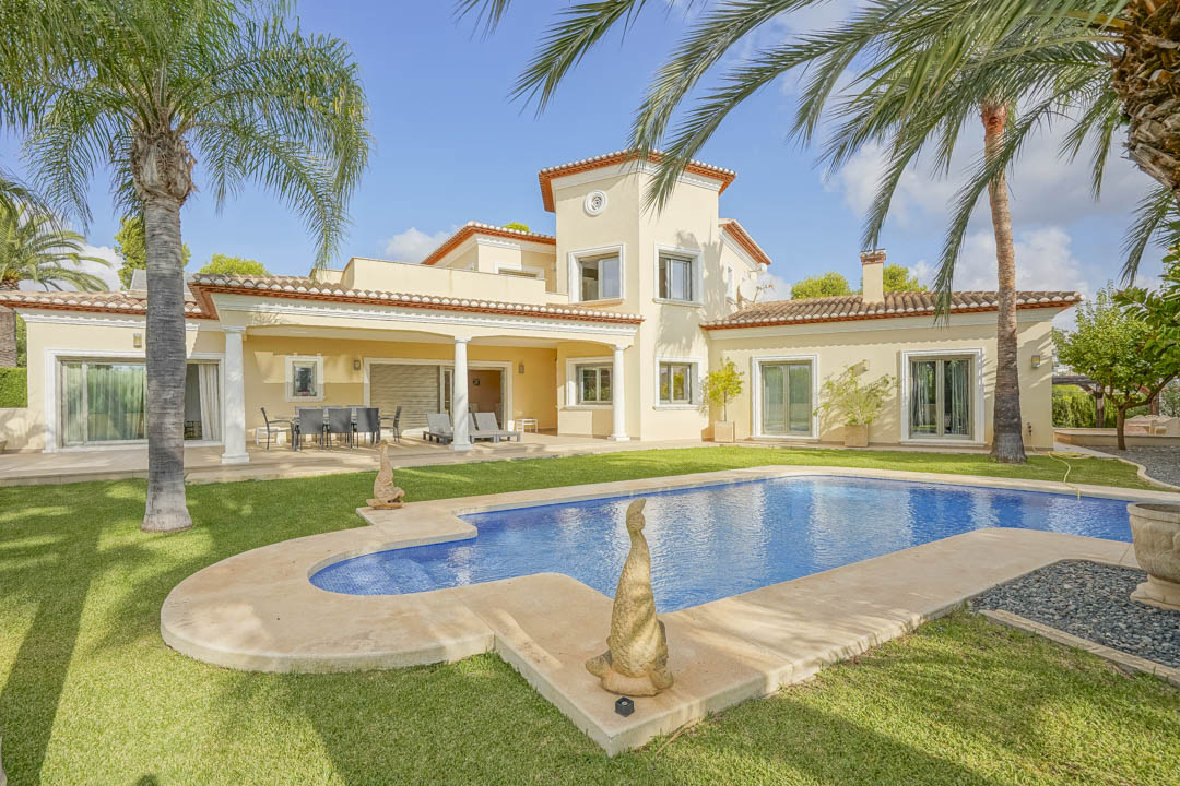 Buitenaanzicht van de villa met privézwembad, volgroeide tuin met palmbomen en een overdekt terras met witte kolommen en traditionele Spaanse architectuur.