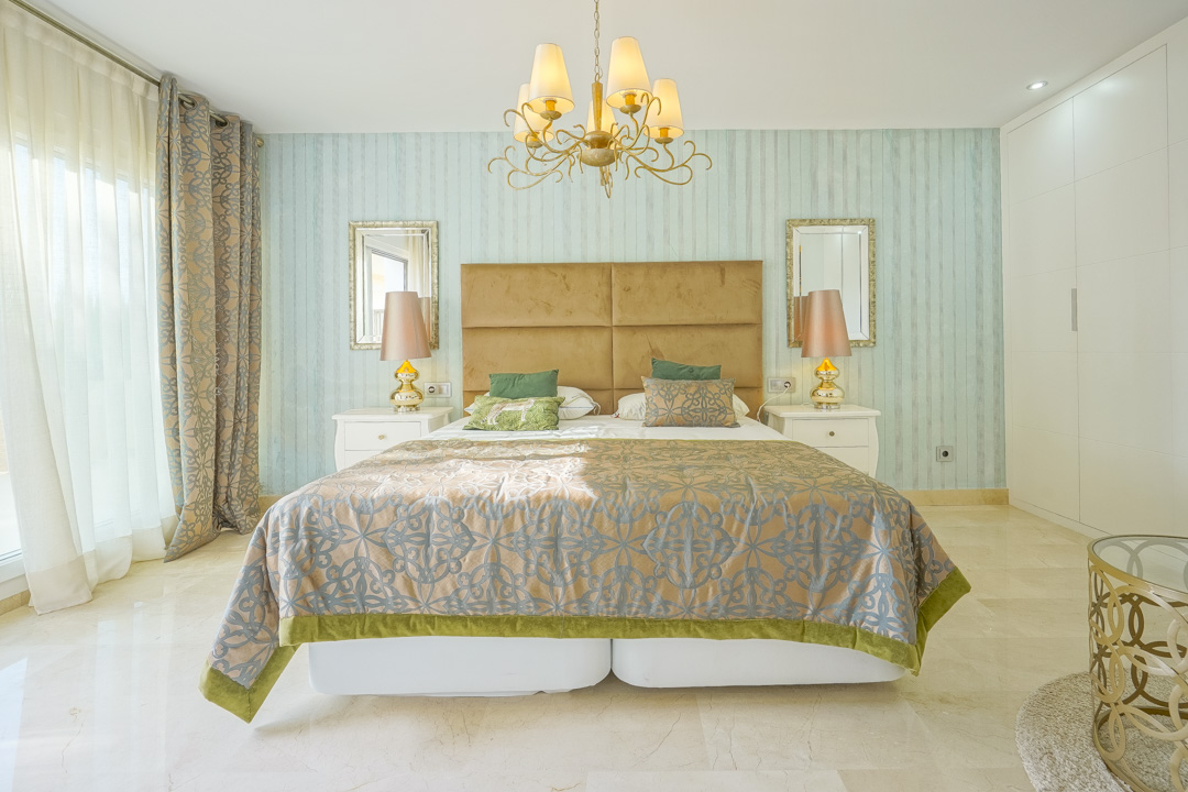 Elegante slaapkamer met turquoise gestreept behang, een mosterdkleurig fluwelen hoofdbord en marmeren vloeren. Voorzien van witte inbouwkasten en veel natuurlijk lichtinval.