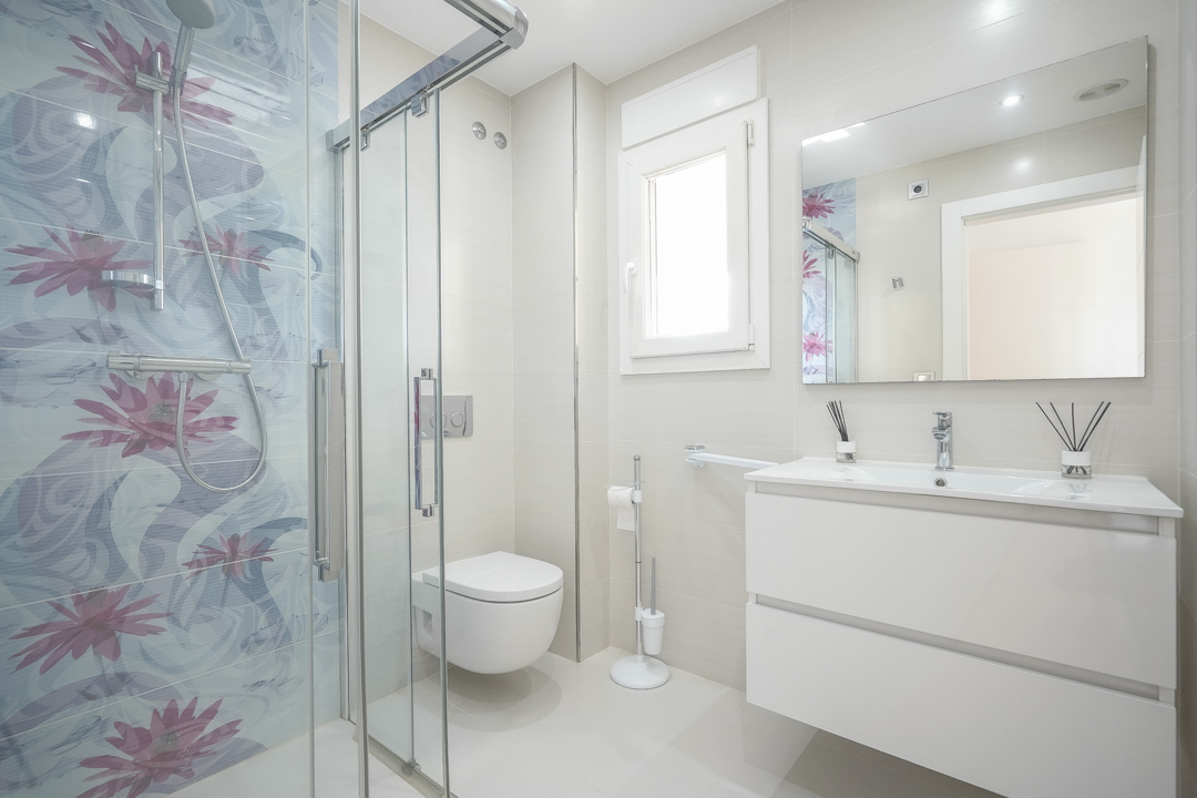 Moderne badkamer met glazen douchecabine voorzien van decoratieve bloementegels, een zwevend wit wastafelmeubel en wandcloset.