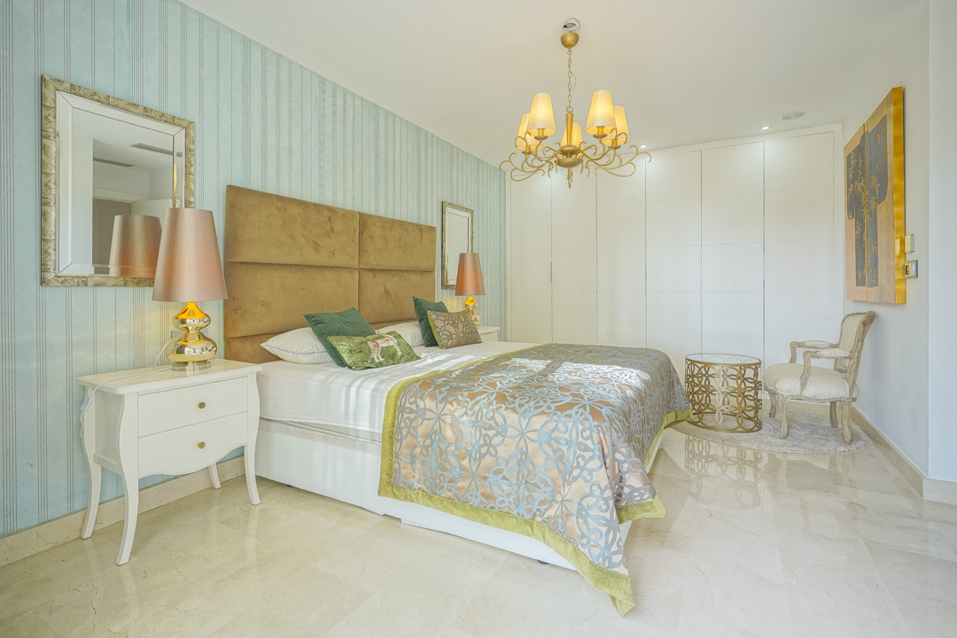 Slaapkamer met blauw gestreept behang, een gewatteerd hoofdbord, gepolijste marmeren vloer en kamerhoge witte inbouwkasten.