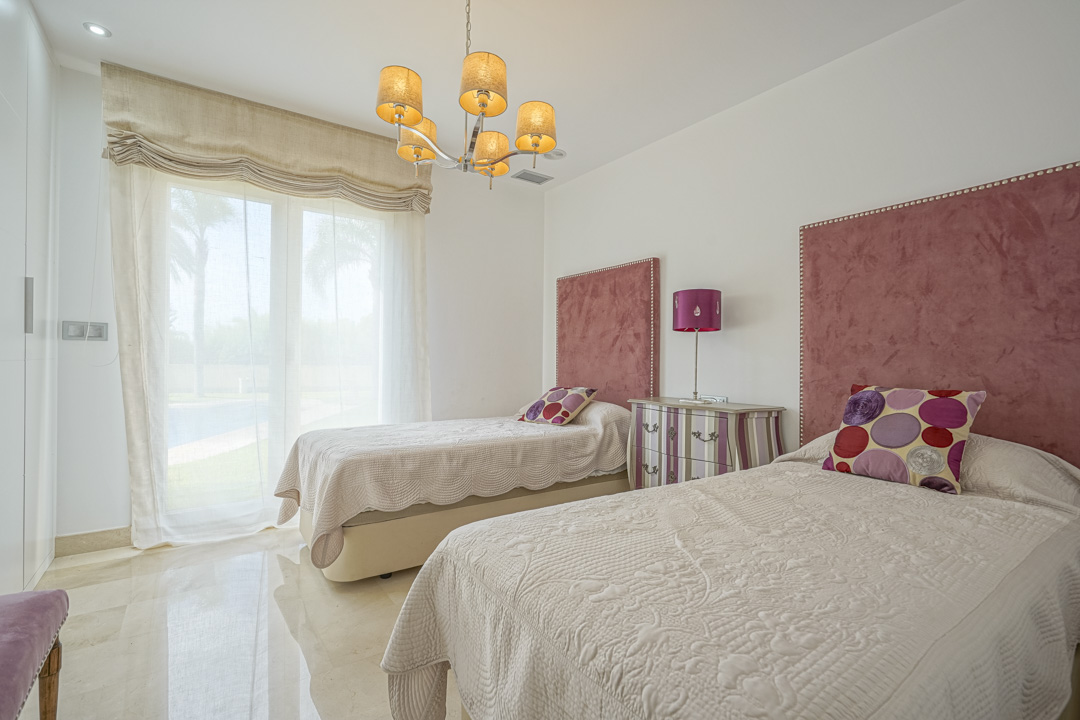 Slaapkamer met twee eenpersoonsbedden, roze fluwelen hoofdborden en directe toegang tot het terras. Voorzien van een gepolijste marmeren vloer en een klassieke kroonluchter.