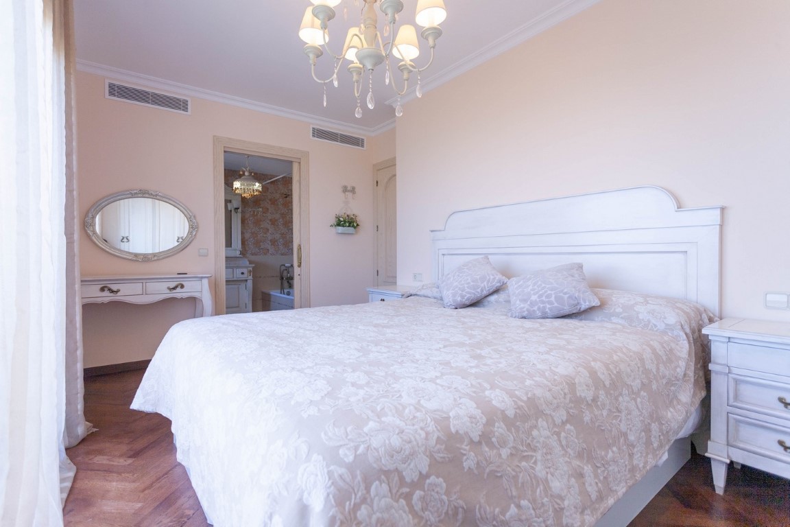 Slaapkamer met wit houten hoofdbord, parketvloer en toegang tot een en-suite badkamer met ligbad en klassieke kaptafel.