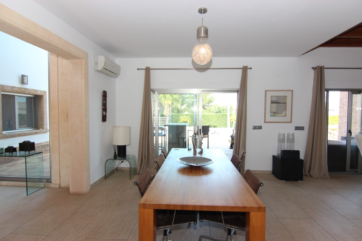 Eethoek met massief houten tafel en keramische tegels, direct verbonden met het buitenterras via grote glazen schuifdeuren.