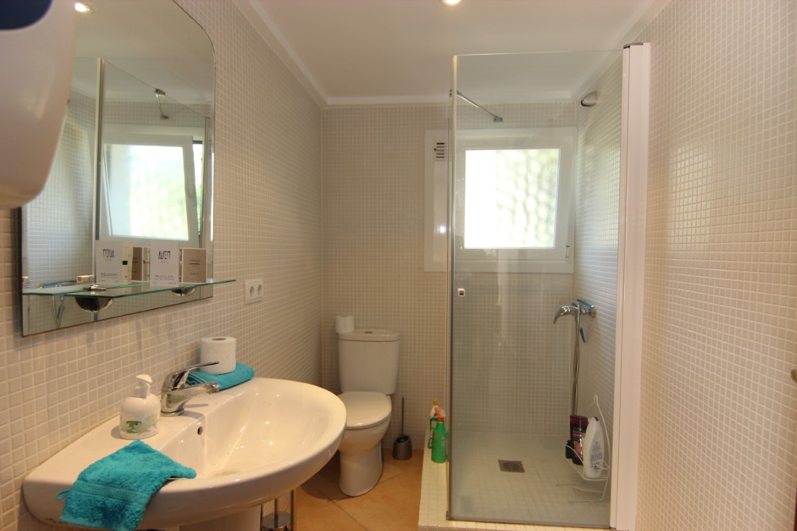 Functionele badkamer met beige mozaïektegels, een inloopdouche met glazen wand en een witte keramische wastafel. Voorzien van een raam voor natuurlijk licht.