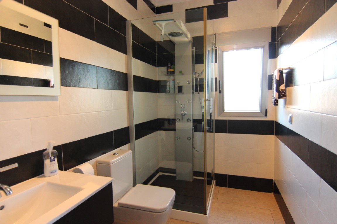 Moderne badkamer met een contrastrijk zwart-wit tegelpatroon, voorzien van een glazen douchecabine met hydromassagekolom en raam.