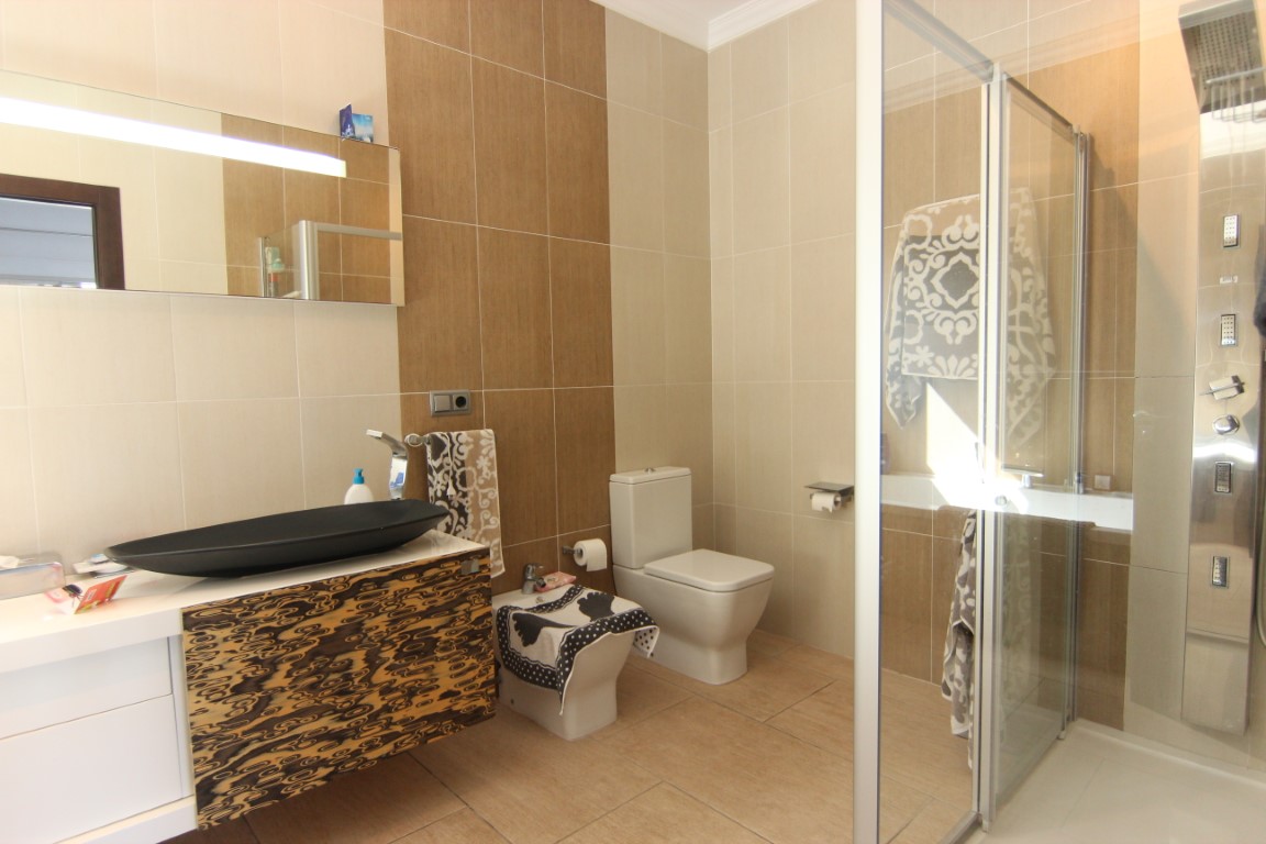 Moderne badkamer met een zwarte opzetwastafel, getextureerd zwevend meubel en een glazen douchecabine met hydromassagepaneel.