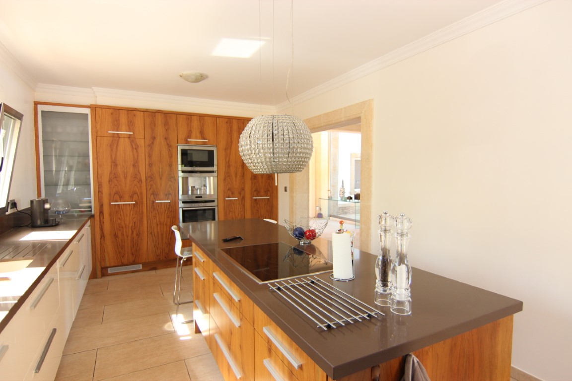 Moderne keuken met kookeiland, bruin werkblad en houten kastenwand. Voorzien van inbouwapparatuur, een inductiekookplaat en een opvallende kristallen hanglamp.