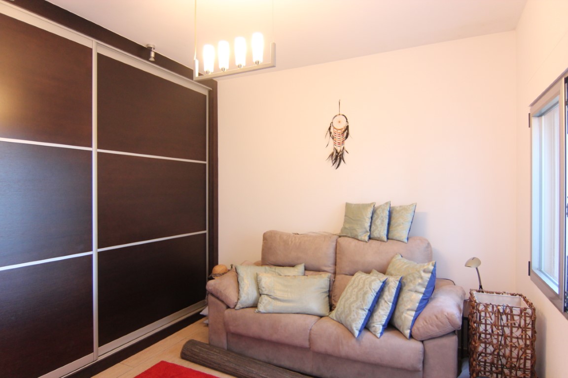 Slaapkamer voorzien van een grote donkerhouten inbouwkast met schuifdeuren, een bank met decoratieve kussens en moderne hangverlichting.