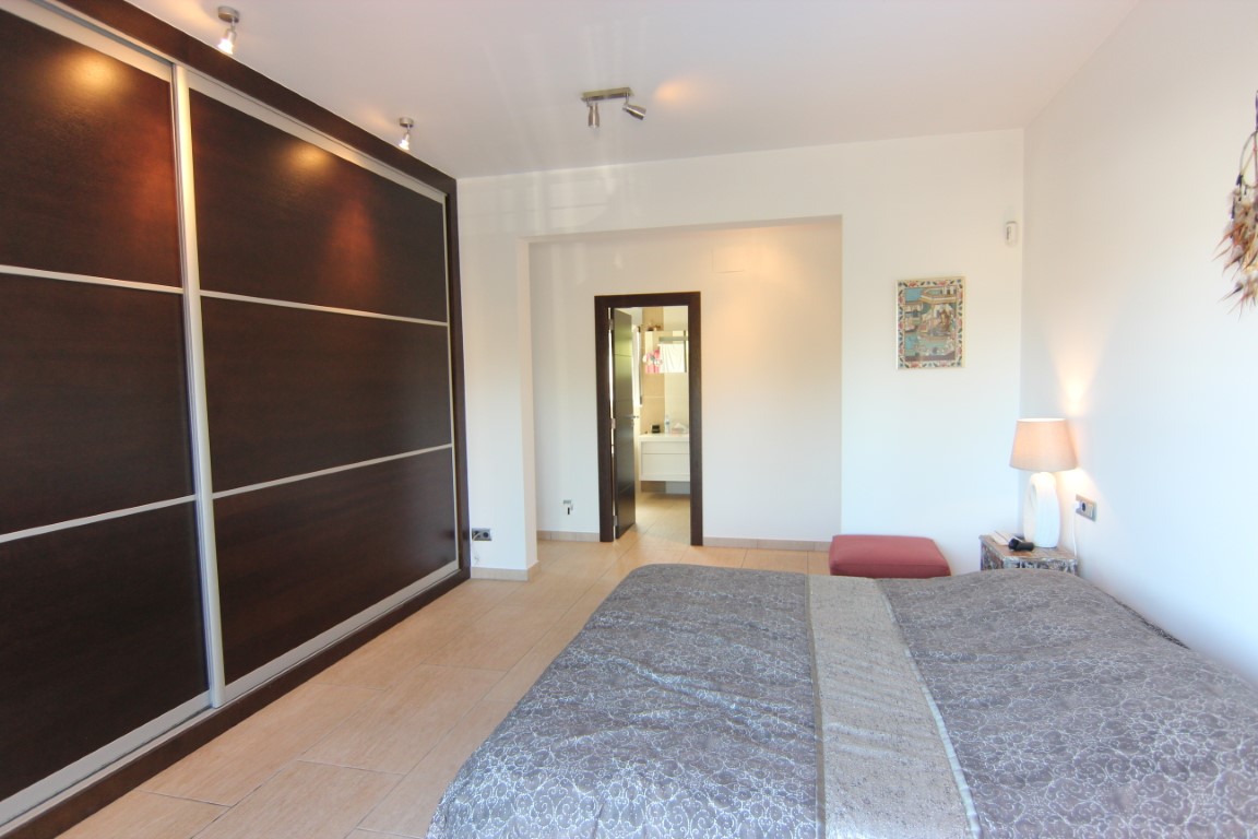 Tweepersoonsslaapkamer met een grote inbouwkast van donker hout en schuifdeuren. De kamer heeft een aangrenzende badkamer en is voorzien van een tegelvloer en inbouwspots.