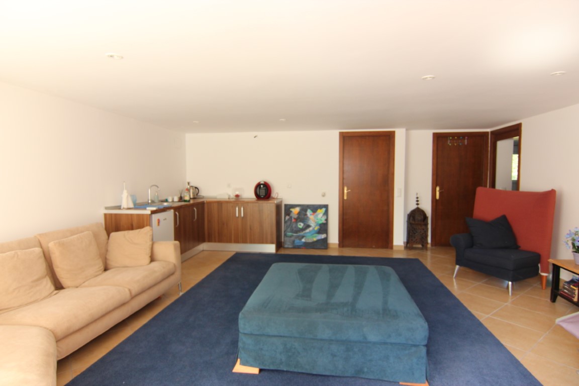 Woonkamer van het gastenverblijf met open kitchenette, inbouwspots, keramische tegelvloer en houten deuren die toegang bieden tot de overige vertrekken.