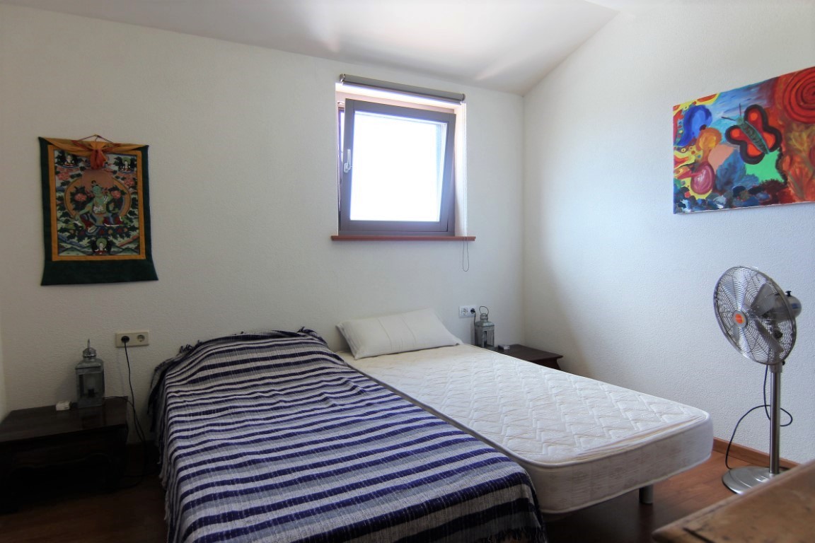 Lichte slaapkamer met twee eenpersoonsbedden, houten vloeren en witte muren versierd met kleurrijke kunst, verlicht door natuurlijk daglicht.