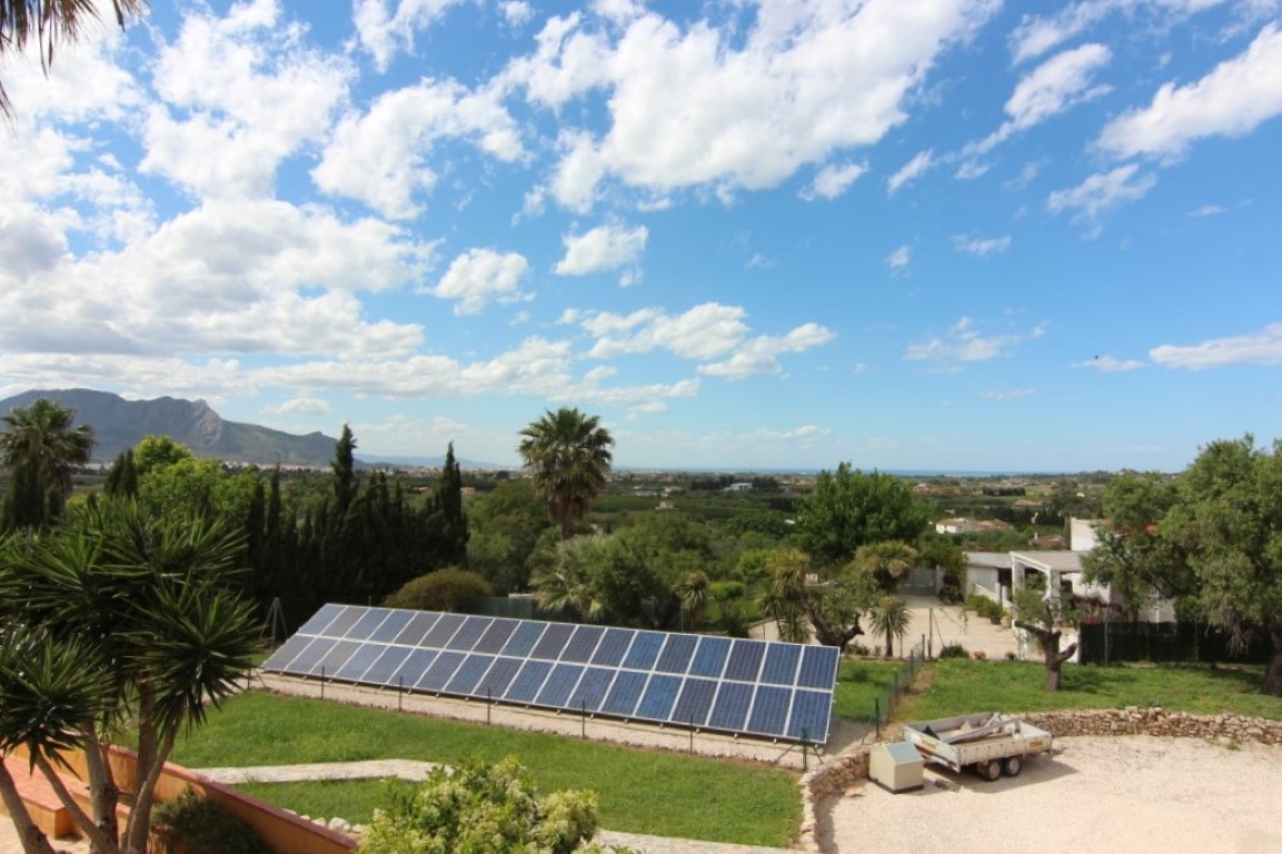 Panoramisch uitzicht op het vlakke perceel met een installatie van zonnepanelen, omgeven door mediterrane beplanting en uitzicht op de bergen en de zee.