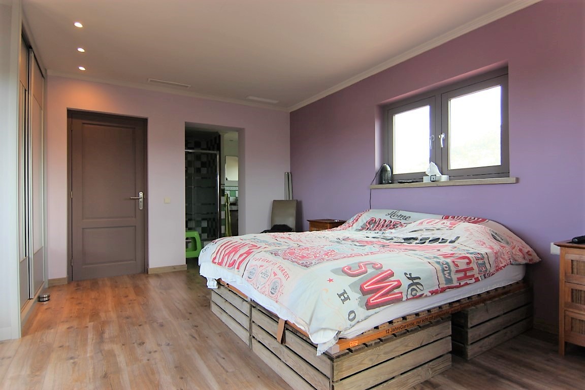 Tweepersoonskamer met lila muren, houten vloer en een bed op een onderstel van houten kratten. Voorzien van inbouwkasten, inbouwspots en een badkamer.