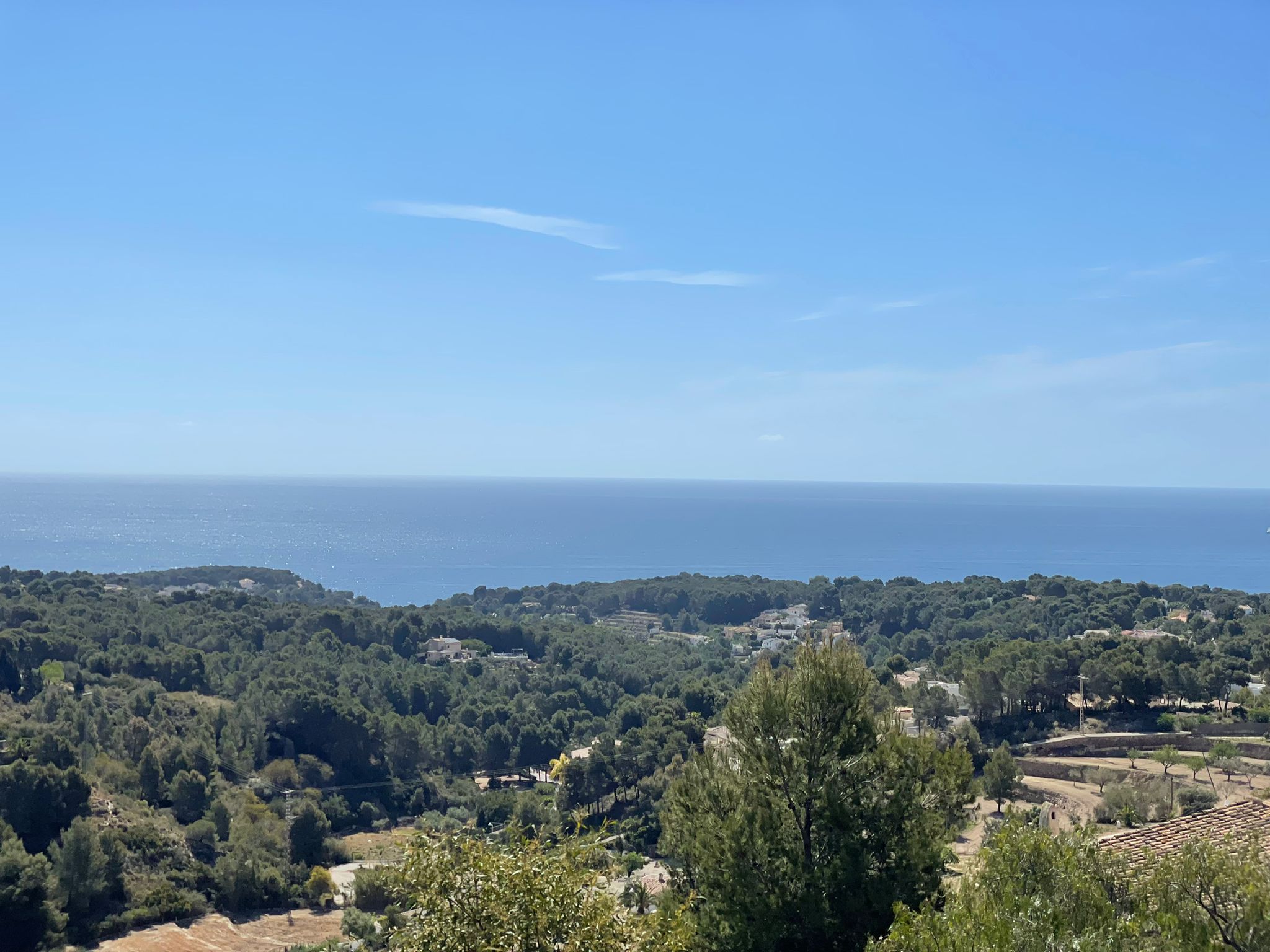 Verhoogd panoramisch uitzicht vanaf het perceel over een dennenbos en de Middellandse Zee die de horizon raakt onder een heldere hemel.