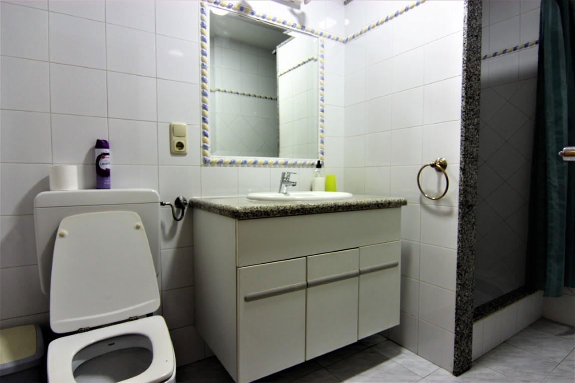 Badkamer met een granieten wastafelblad, spiegel met decoratieve rand en een douche afgewerkt met natuursteen en een douchegordijn.