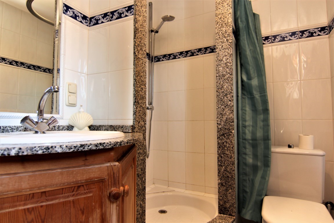 Badkamer met granieten aanrechtblad, houten meubel, geïntegreerde douche met stenen omlijsting en witte wandtegels met blauwe sierrand.