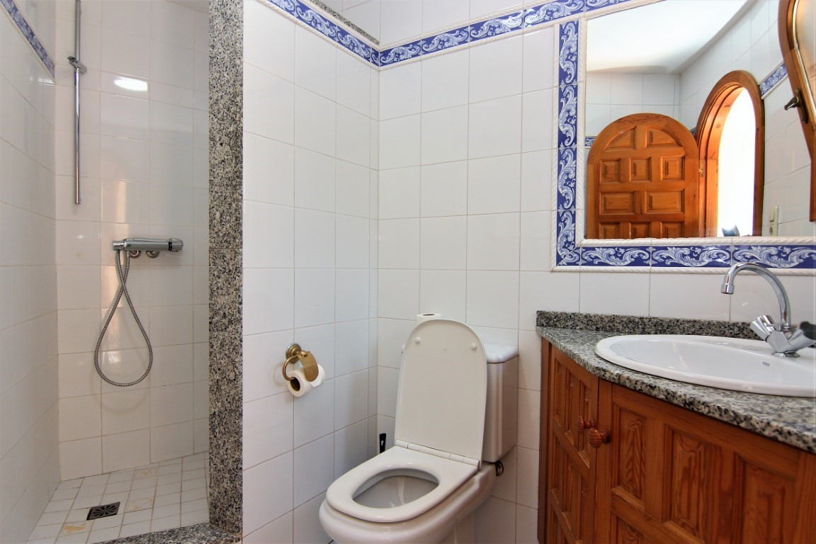 Badkamer met inloopdouche, granieten werkblad, houten meubel en witte tegels met blauwe decoratieve randen.